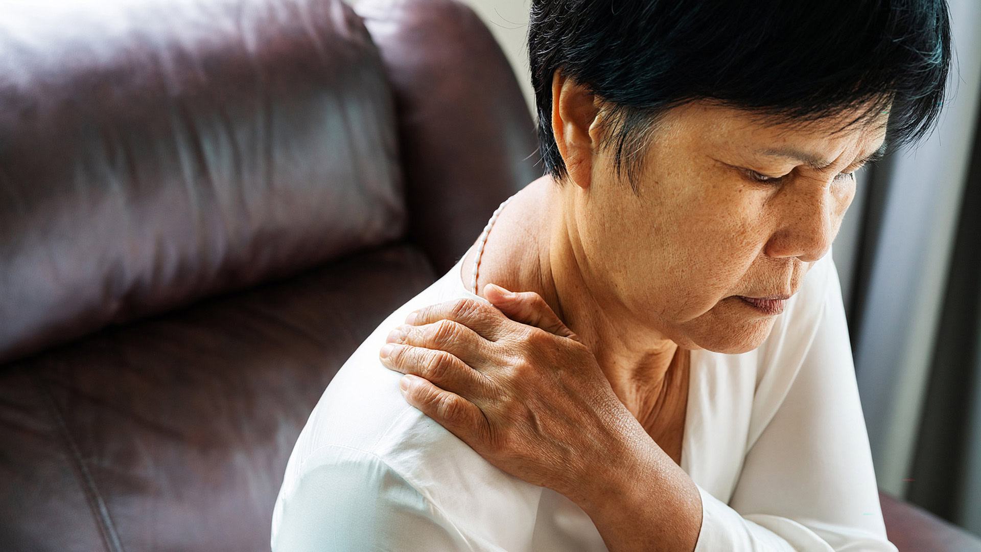 Elderly woman experiencing neck and shoulder pain on couch