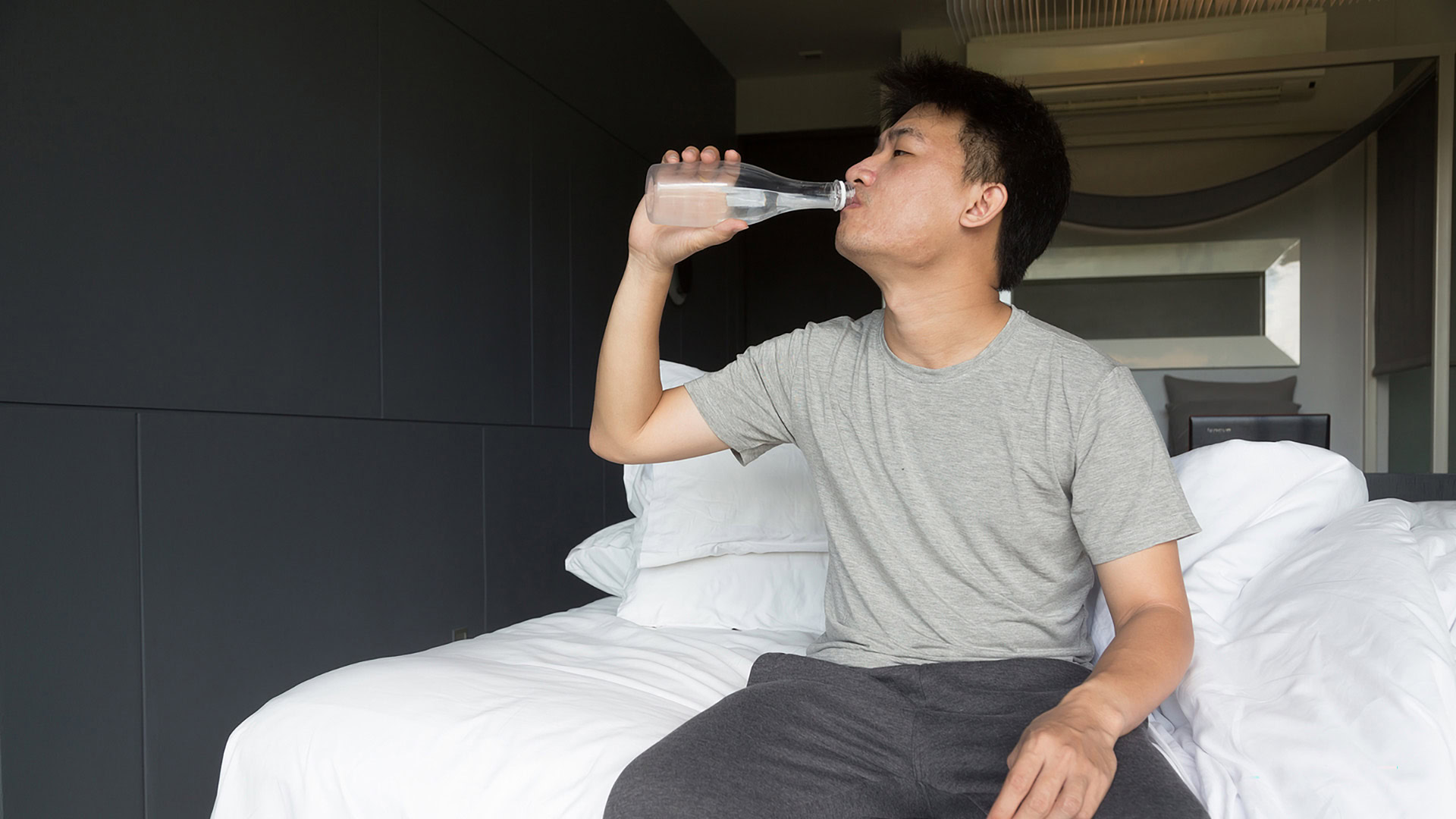A man drinking a bottle of water on bed