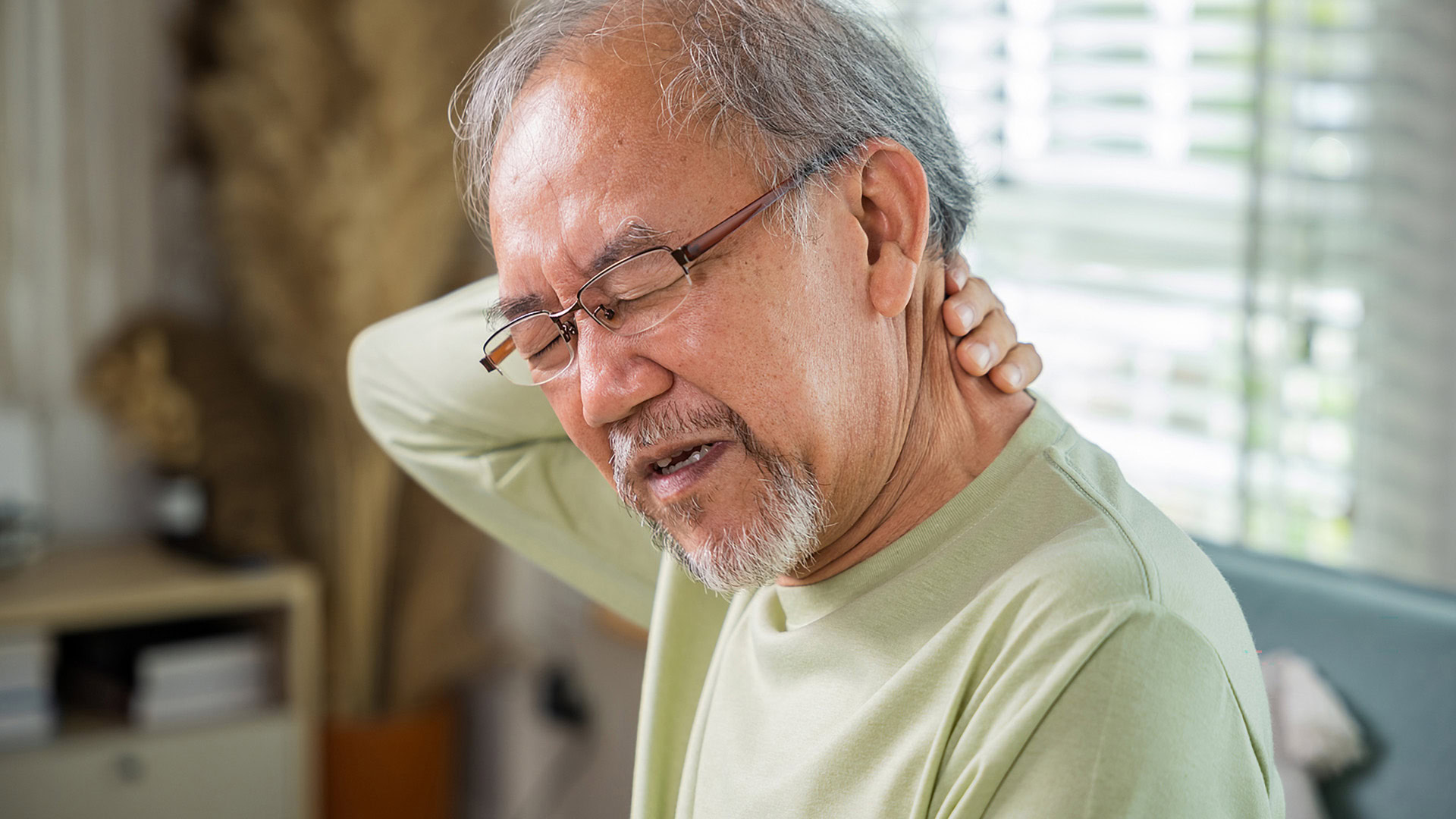 An old man suffering from nape neck pain at home